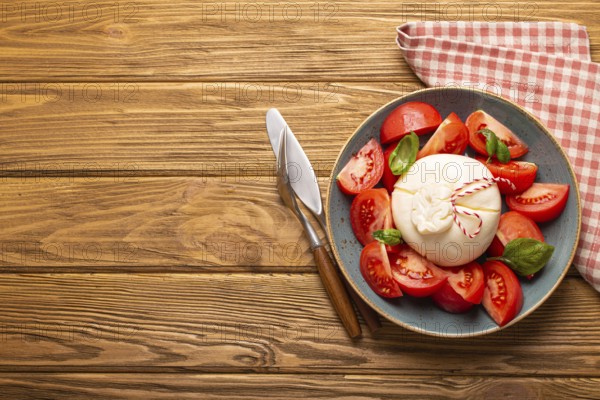 Italian salad with fresh tomatoes, burrata cheese, basil and olive oil served on ceramic plate on