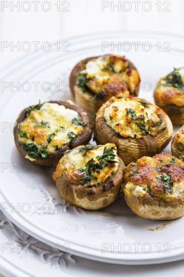 Baked champignons mushrooms, filled with cheese, parsley and roasted garlic on white plate.