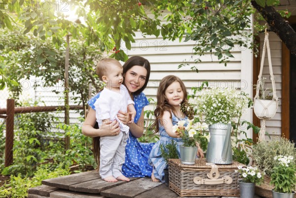 Young delighted mother sitting in armchair with adorable little siblings on terrace of country