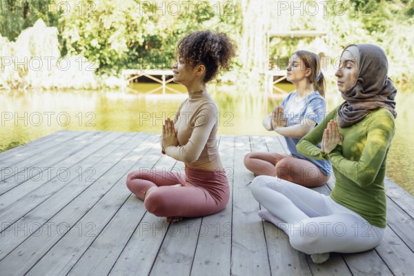 Group of teenages is engaged in fitness on pier by the lake or river. Young and positive girls go