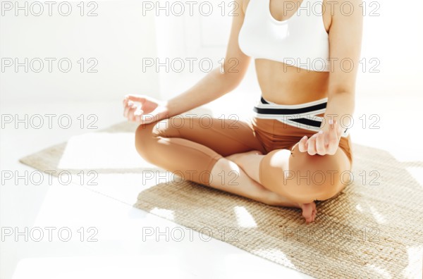 Back view of unrecognizable female in sportswear sitting with crossed legs and mudra hands on mat