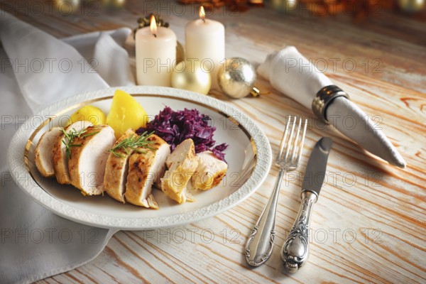Roast chicken breast with red cabbage and potatoes on a white plate, silverware and napkin on a