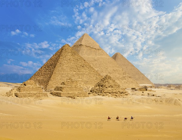 All Egyptian Pyramids from distance with row of camels walking in foreground in Giza, Cairo, Egypt.