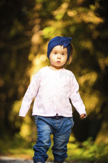 Portrait of 2 years old baby girl in forest walking by herself. Not wanting to follow parents.
