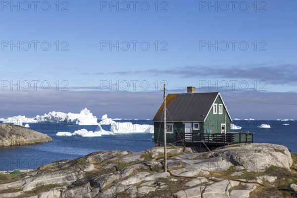 Qeqertarsuaq, Greenland, July 05, 2018: A green wooden house with icebergs in the background, North