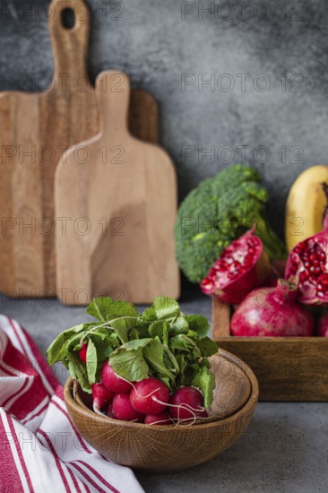 Bunch of fresh raw radish in wooden bowl on kitchen table with fresh fruit, greens, vegetables in