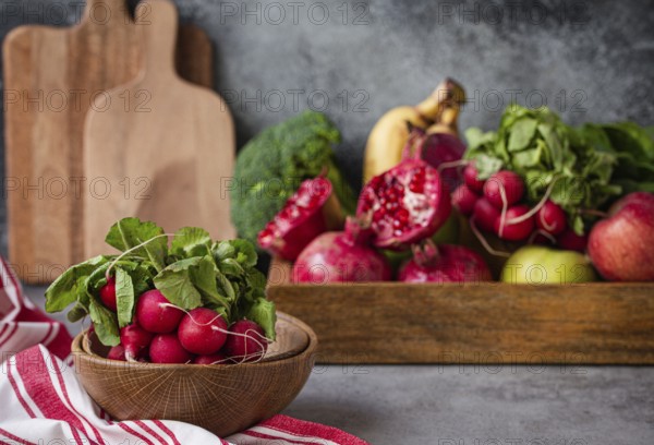 Bunch of fresh raw radish in wooden bowl on kitchen table with fresh fruit, greens, vegetables in