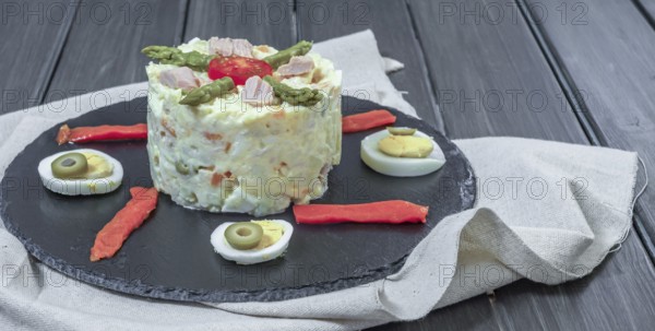 Black slate plate with ensaladilla rusa or Russian salad typical spanish tapa garnished with red