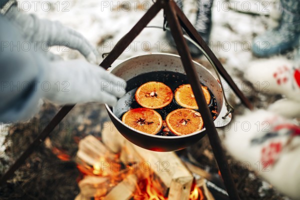 From above traditional mulled wine with slices of orange preparing in pot over burning logs in