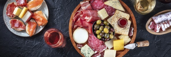 Italian antipasti or Spanish tapas panorama on a black background. Gourmet cold meat and cheese