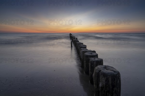long exposure view of an ocean sunset with sandy beach and wooden pylon storm groin in the