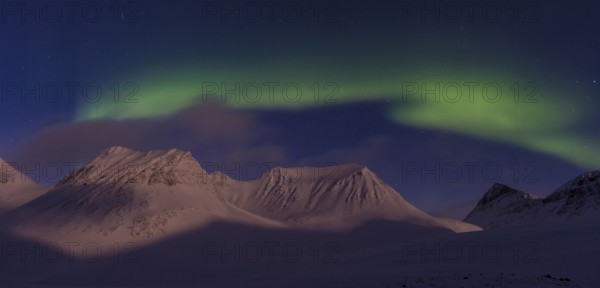 Northern Lights (Aurora borealis) over moonlit mountains in the valley Stuor Reaiddavaggi,