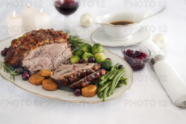 Roast pork ham with crust, green beans, Brussel sprouts, carrots, cranberry and sauce on white