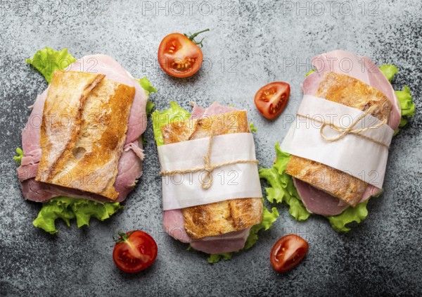 Fresh ciabatta sandwiches with ham, cheese, lettuce, tomatoes on stone concrete background,