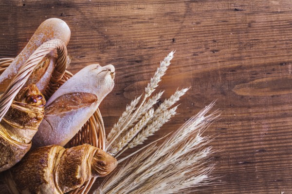 Close up view on baguettes and croissants in wicker basket with ears of wheat on old wooden boards