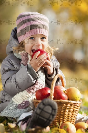 Happy kid eating red apple in autumn park. Healthy lifestyles concept