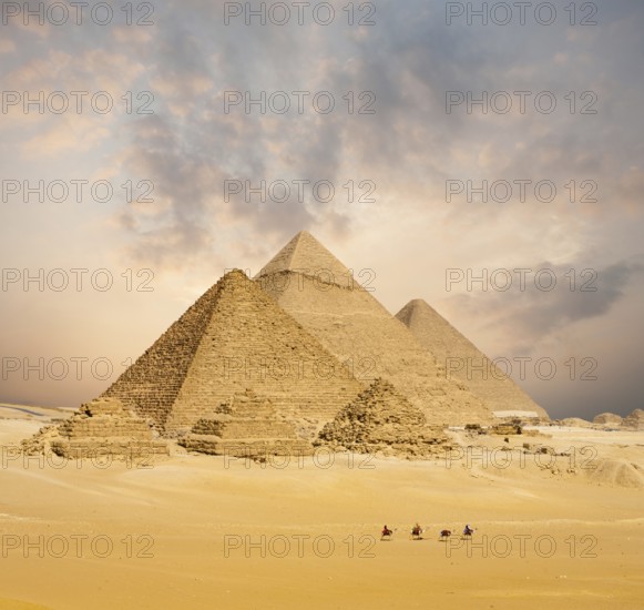 Dramatic sunset behind all distant Egyptian Pyramids together with line of camels walking in