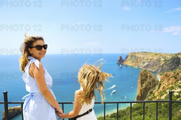 Mother and little girl standing next to fence on viewpoint and admiring picturesque view of rocky