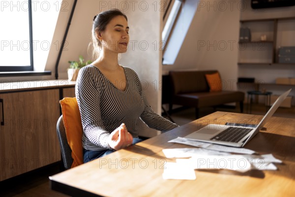 Stress relief during freelance work. Brunette woman freelancer sitting in lotus pose and meditating