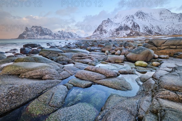 Rocks on beach of fjord of Norwegian sea in winteron sunset. Utakliev beach, Lofoten islands,