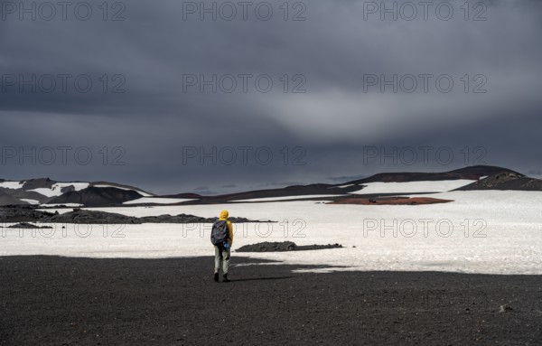 Hikers in snow-covered volcanic landscape with volcanic sand and petrified lava, crater of Askja