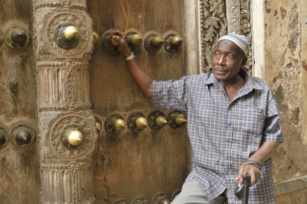 Elderly man leaning against a wooden door in the historic town centre, Zanzibar City, Zanzibar,