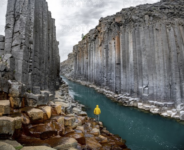 Tourist standing by the river in Stuðlagil Canyon, turquoise blue river between basalt columns,