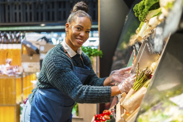 African american saleswoman wearing plastic gloves arranging organic asparagus at the vegetable