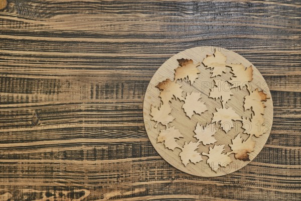 A circular wooden base hot pad displays intricately cut wooden leaves with varying hues, arranged
