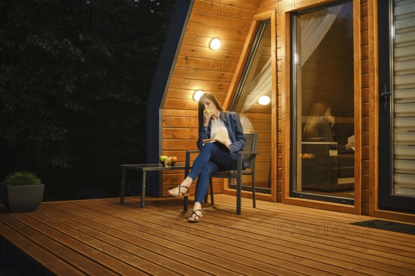 Late in the evening, a young woman sits on the terrace of a country house, eats an apple and reads