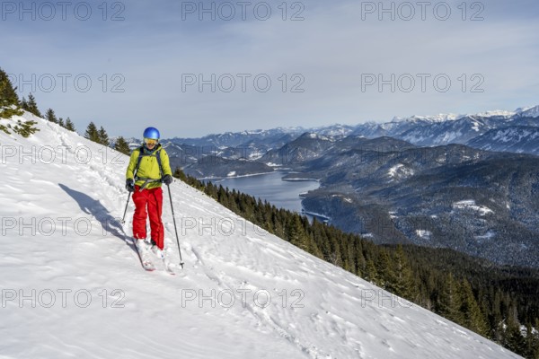 Skiers skiing down the Simetsberg, view of Walchensee and mountain panorama, Estergebirge, Bavarian