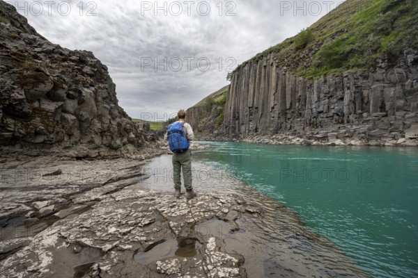 Tourist standing by the river in Stuðlagil Canyon, turquoise blue river between basalt columns,