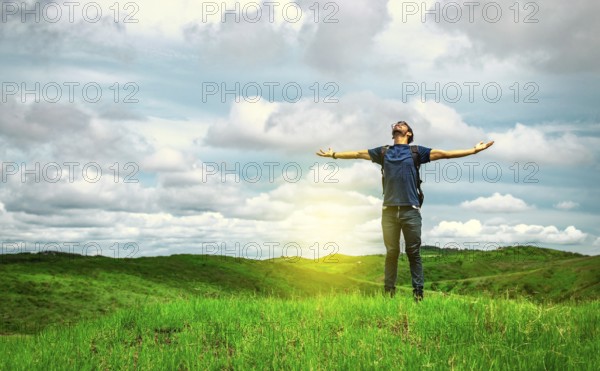 Adventurous man spreading his arms in the countryside. Man with backpack on a hill spreading his