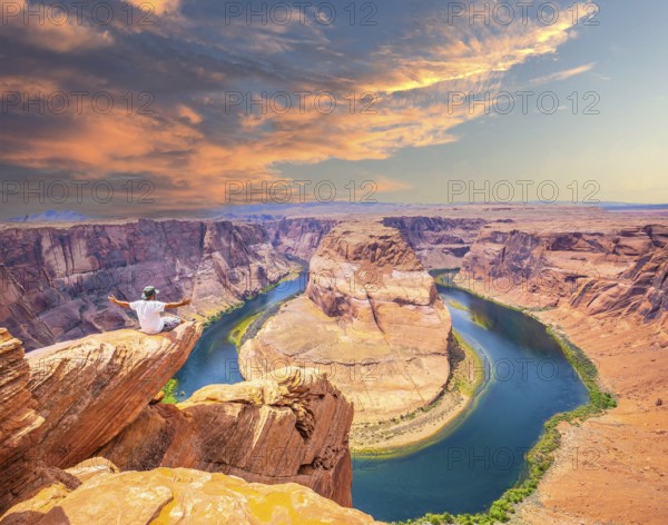 A young man sitting with a white shirt and green pants on Horseshoe Bend and the Colorado River in