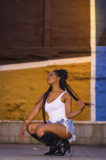 Fashionable urban style with an African girl with braids on a street in the city at night. White