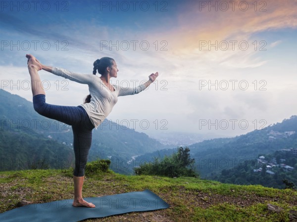 Woman doing yoga asana Natarajasana, Lord of the dance pose outdoors at waterfall in Himalayas