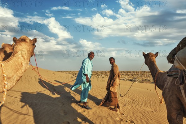 Rajasthan travel background, two indian cameleers (camel drivers) with camels in dunes of Thar