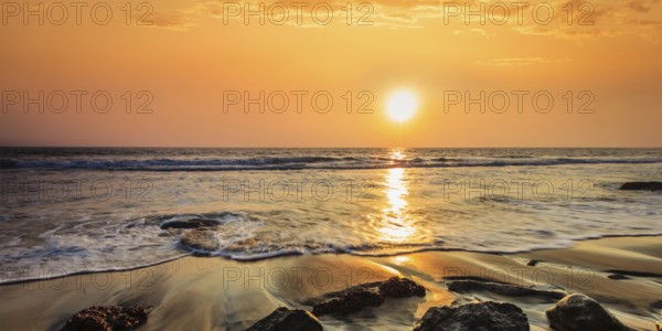 Tropical beach vacation background, panorama of waves and rocks on beach on sunset with beautiful