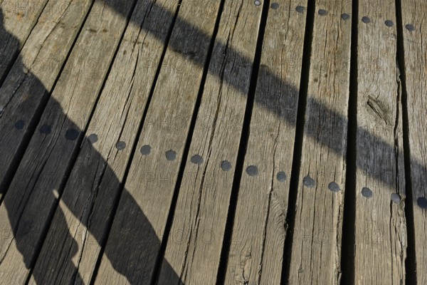 Shadow cast by a person and wooden planks, heritage-protected wooden bascule bridge over the Trebel