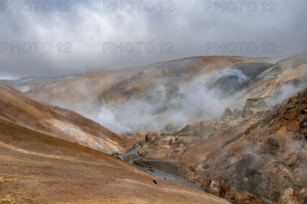 Steaming stream between colourful rhyolite mountains and snowfields, Hveradalir geothermal area,