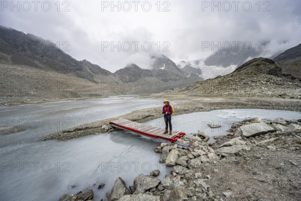 Mountaineer on a bridge over a glacial river of the glacier Glacier de Cheilon, Valais, Western
