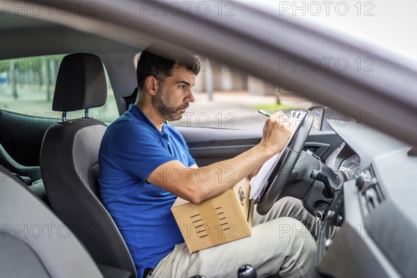 Side view from inside a vehicle of a serious delivery man writing and inventorying packages on a