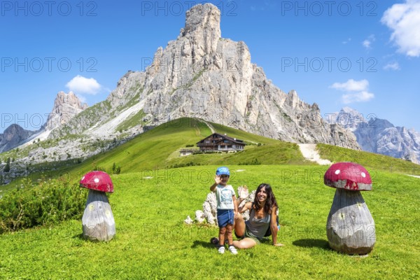 Mother and son waving near big wooden mushrooms with scenic view of nuvolau peak and mountain hut