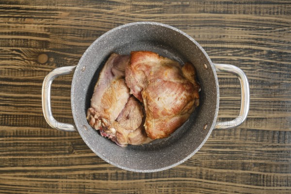 Tender, cooked turkey meat sit in a silver pot on a rustic wooden table, showcasing their golden