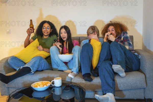 Four friends experiencing different emotions while watching a suspenseful movie at home, enjoying