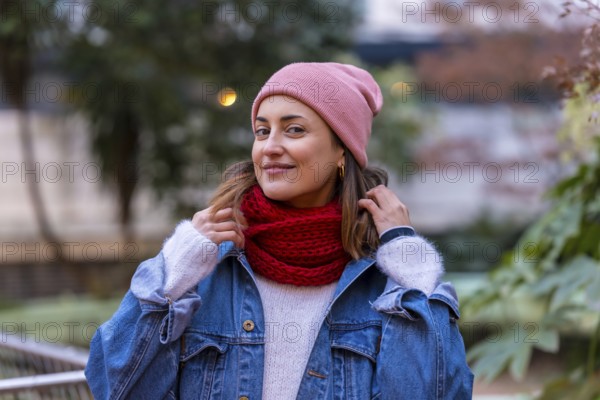 Happy woman wearing stylish winter clothes, playfully adjusting her red scarf while enjoying a