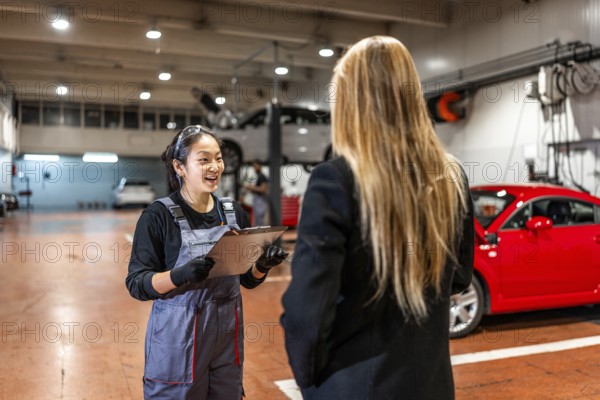 Smiling female mechanic explaining repair details to a customer while delivering a car in a modern