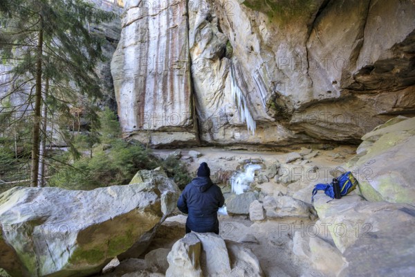 Hiker taking a break, frozen waterfall with icicles in the Gautschgrotte, Hohnstein, Saxony,