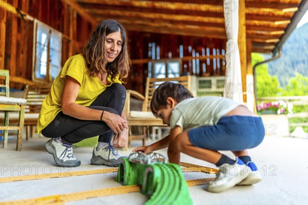 Mom and child enjoying playtime together, building a car track on the porch of their cozy wooden
