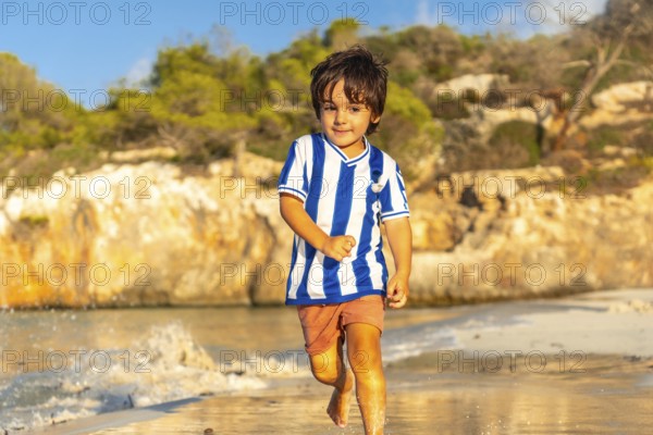 A young boy is running on the beach wearing a striped shirt and shorts. The image has a light and
